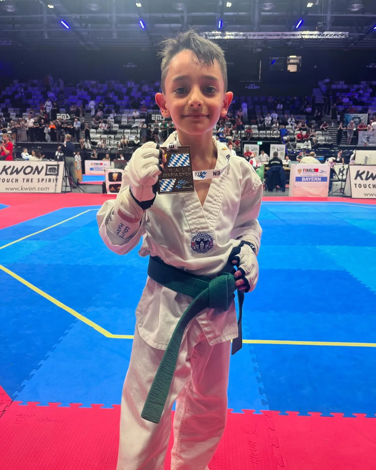 Eine junge Black-Tiger-Sportlerin hält ihre Medaille vor der Wettkampffläche hoch