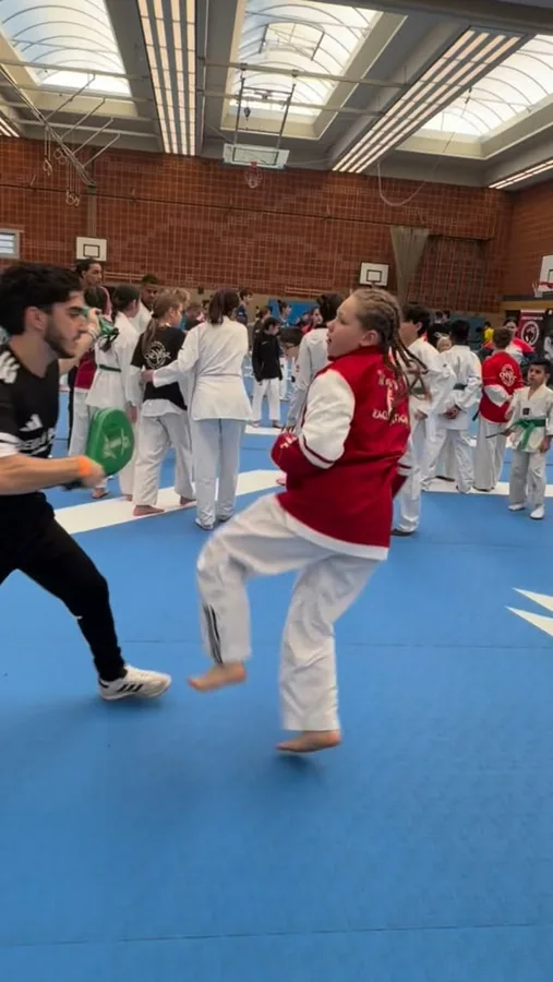 Ein Kind übt mit einem Trainer einen Tritt auf die Pratze.