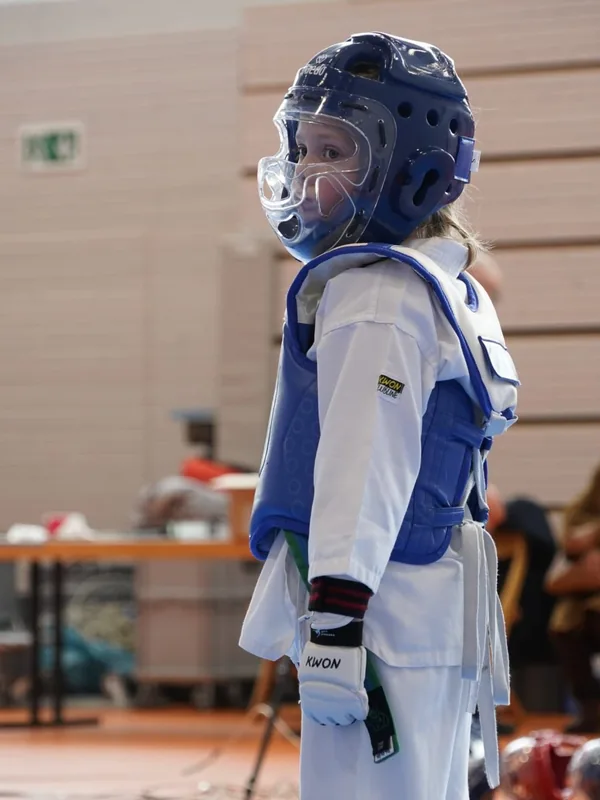 Ein junger Sportler steht mit blauem Körperschutz und Schutzhelm auf der Matte.