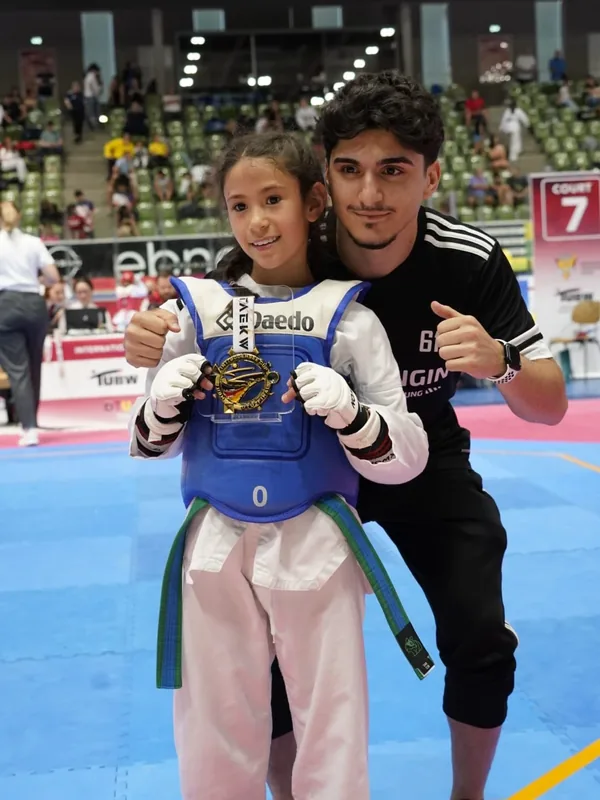 Eine junge Black-Tiger-Sportlerin zeigt mit ihrem Trainer ihre Medaille beim Bodensee Cup.