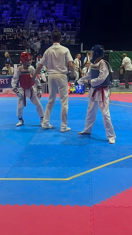 Zwei Sportler üben Sparring mit Schutzkleidung auf einer blauen Wettkampfmatte.