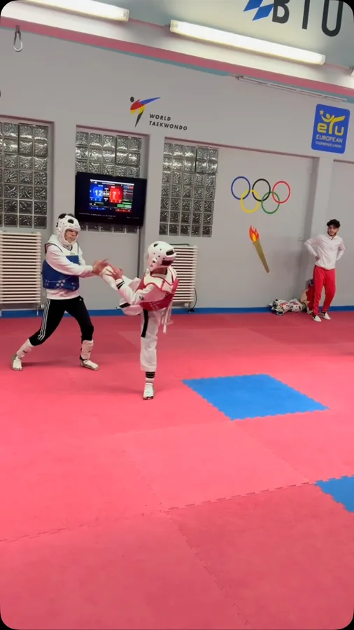 Zwei junge Sportler üben auf der roten Trainingsmatte Sparring mit Schutzausrüstung.