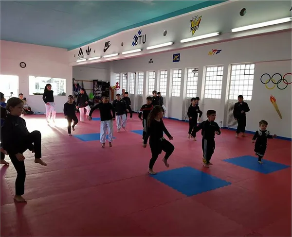 Kinder üben gemeinsam Kniehebeläufe auf der Taekwondo-Matte.