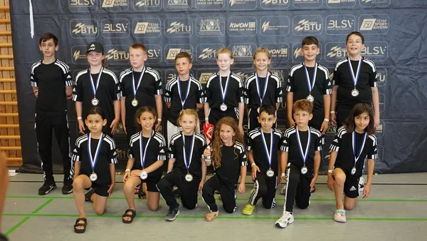 Das Black-Tiger-Team steht mit Medaillen für ein Gruppenfoto in einer Sporthalle zusammen.