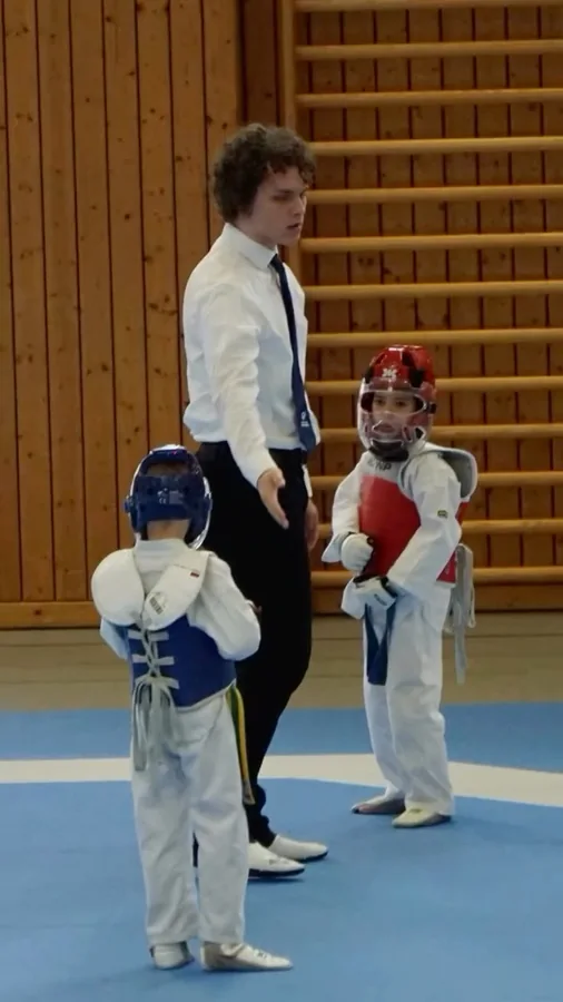 Zwei Kinder mit Helm und rotem beziehungsweise blauem Körperschutz erhalten vor ihrem Kampf letzte Hinweise.